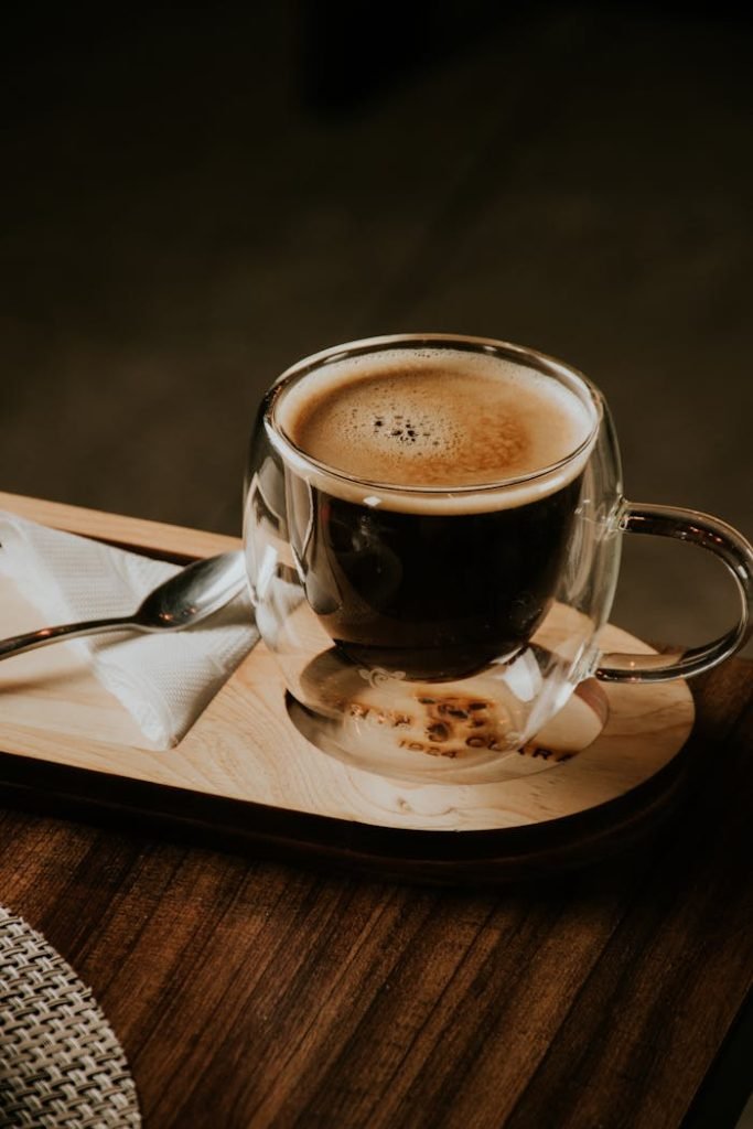 Double-walled glass mug with rich espresso on wooden tray in a cozy setting.